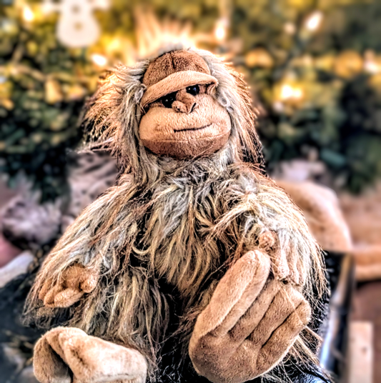 Plush toy resembling a creature with long hair against a blurred Christmas tree background